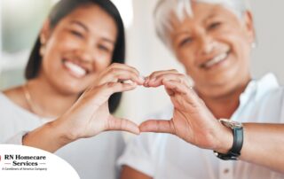 A daughter and an older mother create a heart with their hands, representing the feeling that is highlighted during National Family Caregivers Month