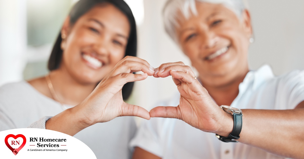 A daughter and an older mother create a heart with their hands, representing the feeling that is highlighted during National Family Caregivers Month